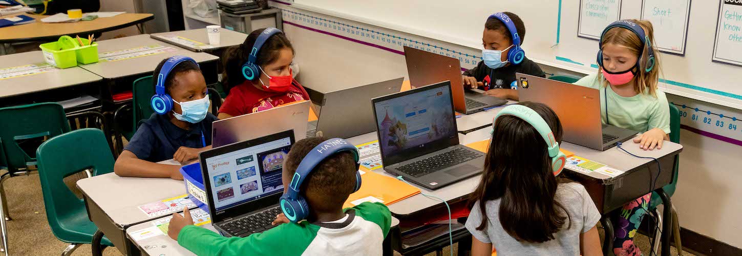 Students in class wearing headphones and using laptops